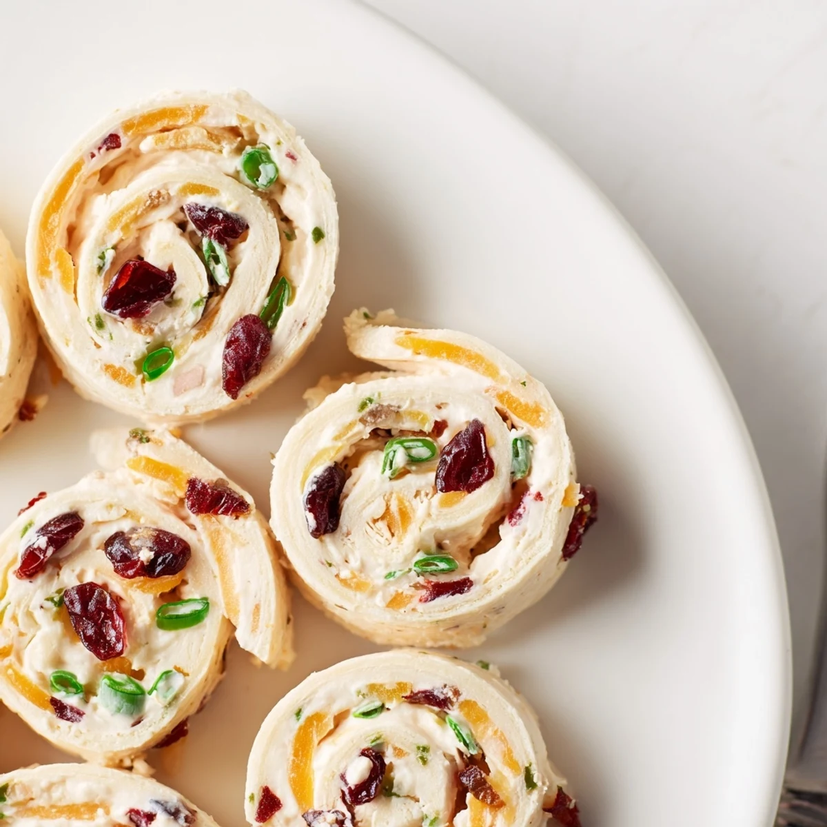 Delicious cranberry jalapeño cream cheese pinwheels garnished with fresh green onions and herbs.