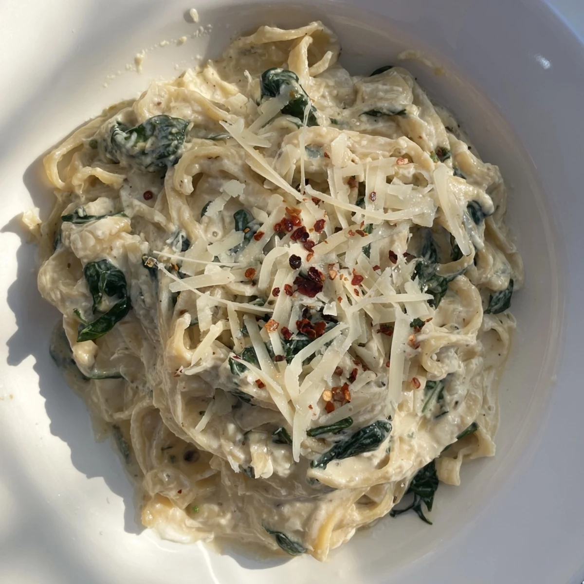 Deliciously light Lighter Fettuccine Alfredo with Spinach, garnished with parmesan and red pepper flakes.