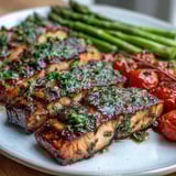 Freshly grilled lemon herb salmon fillets resting beside tender asparagus and blistered cherry tomatoes on a rustic platter.