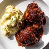 Tender honey BBQ chicken thighs, with a rich, smoky glaze, next to a bowl of creamy garlic mashed potatoes.