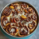 Melted butter and brown sugar glaze coats Peach Cobbler Cinnamon Roll Casserole.