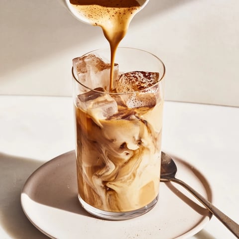 Rich tahini iced coffee topped with plant-based milk and ice cubes.  