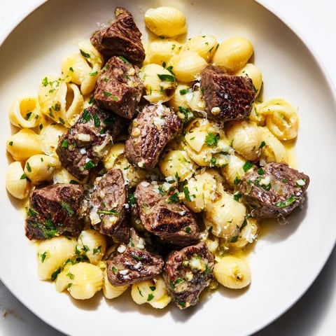 Golden-brown garlic butter steak bites nestled over creamy, cheesy pasta shells, a comforting dinner.