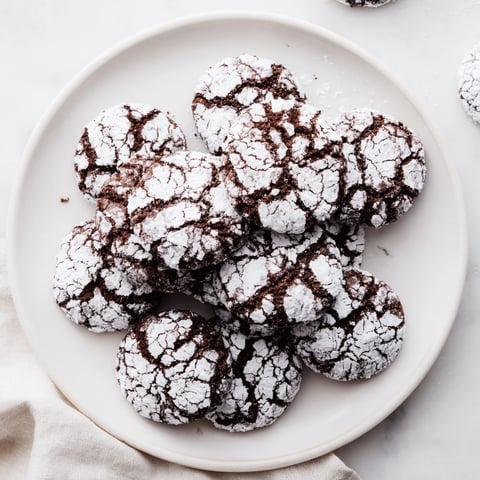 Warm, crackled Chocolate Crinkle Cookies, dusted in powdered sugar, ready to enjoy with milk.