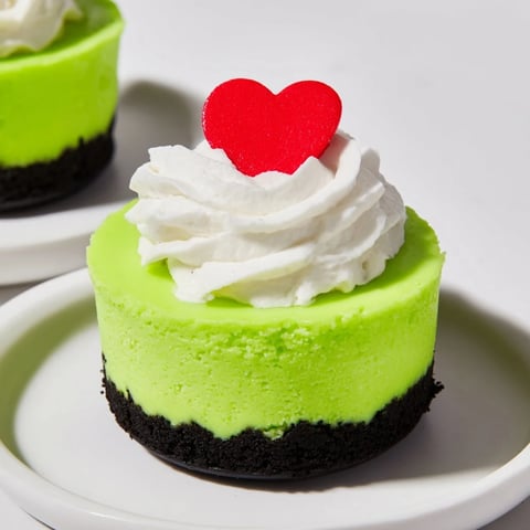 Festive Grinch Mini Cheesecakes topped with whipped cream and red heart sprinkles, a perfect holiday dessert.