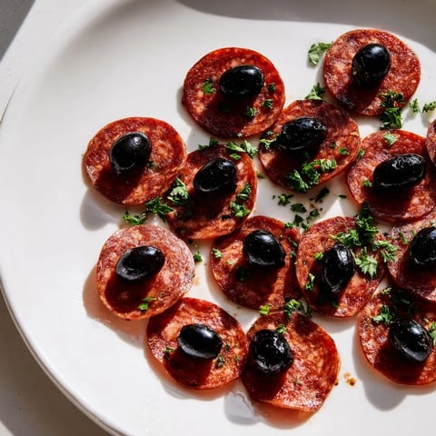 Sliced pepperoni and olive halves appetizer, showcasing savory pepperoni topped with glistening olive halves.