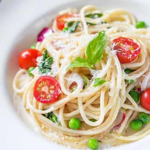 Fresh Spring Veggie One-Pot Spaghetti simmered with peas and tomatoes, topped with Parmesan and basil.