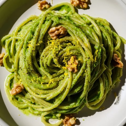Creamy Spinach Walnut Pasta served in a white bowl, with glossy green sauce clinging to penne and toasted walnut pieces on top.  
