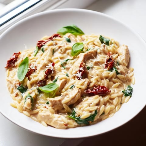 Creamy Tuscan Chicken Orzo in a skillet, topped with fresh basil and melted Parmesan, ready to serve.