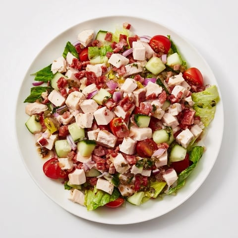 A close-up of the vibrant Italian Deli Chopped Chicken Salad, featuring juicy chopped chicken, salami, and provolone on crisp romaine lettuce, drizzled with a tangy herb dressing.  