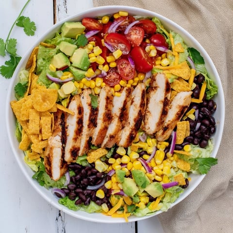 A vibrant Honey Lime Chicken Taco Salad with grilled chicken, romaine, corn, black beans, and avocado, served with tortilla strips.  