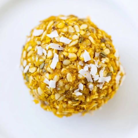 Freshly rolled Ginger Turmeric Energy Balls, dusted with shredded coconut and resting on a marble surface for a healthy snack.