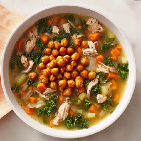 A comforting spoonful of flavorful Chicken Kale Soup, garnished with golden, crunchy chickpeas and fresh herbs.