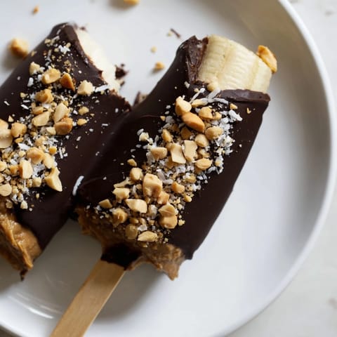 Homemade Frozen Banana Chocolate Pops, richly coated in dark chocolate and sprinkled with crunchy peanuts and coconut.