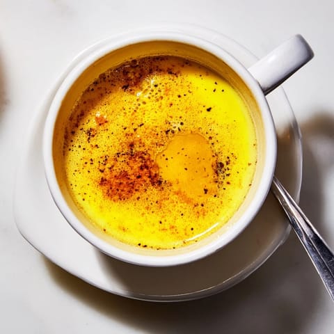 Two mugs of golden milk on a wooden table, showcasing the vibrant yellow hue and aromatic spices perfect for a calming bedtime beverage.