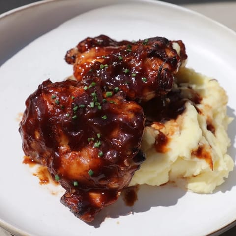 Crispy skin honey BBQ chicken thighs, glistening with sauce, served alongside fluffy garlic mashed potatoes.