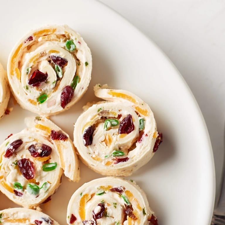 Delicious cranberry jalapeño cream cheese pinwheels garnished with fresh green onions and herbs.