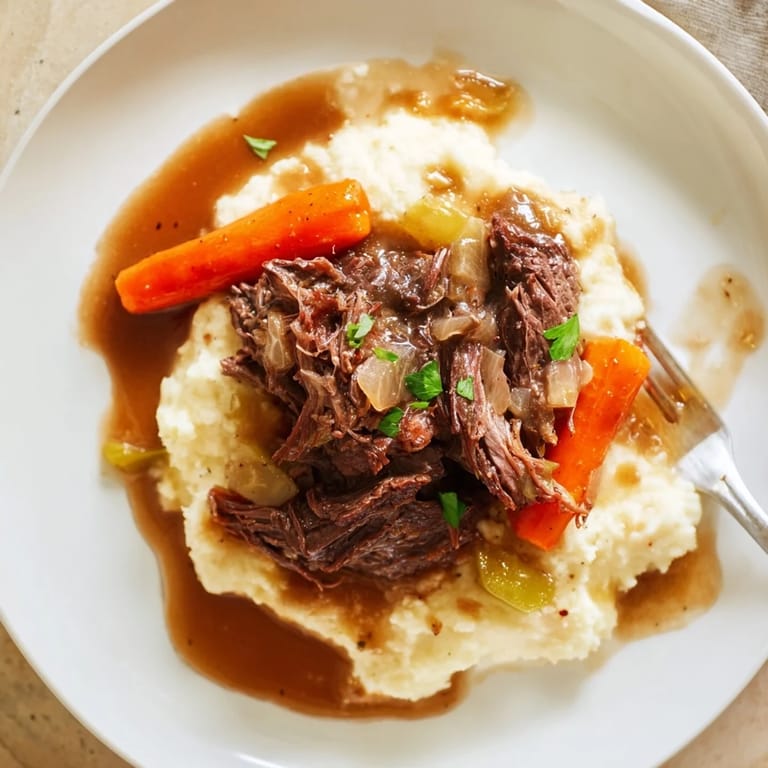 A hearty dish of slow cooker pot roast served atop buttery mashed potatoes, perfect for dinner.  