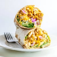 A close-up of a Buffalo Ranch Chicken Wrap sliced in half, revealing layers of shredded chicken coated in spicy red sauce, crisp romaine lettuce, and melted cheddar cheese. 