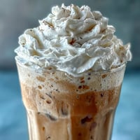 Creamy iced vanilla bean frappuccino blended with coffee and almond milk, topped with fluffy coconut whipped cream.