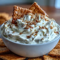 Creamy cheesecake dip with graham crackers, perfect for parties, served in a bowl with crunchy dippers on the side.
